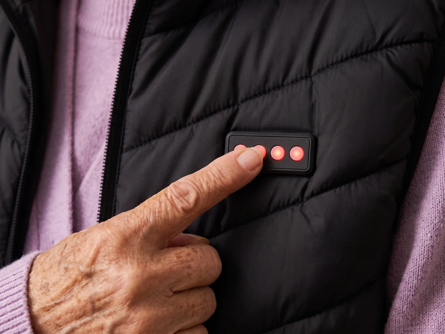 Close-up of an older woman's finger pressing the small four-button panel on the chest of the black quilted vest